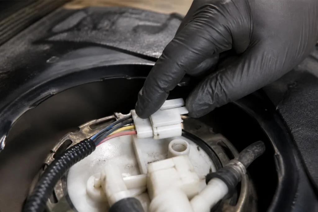 Technician releasing the lock tab on a fuel pump module electrical connector in a shop